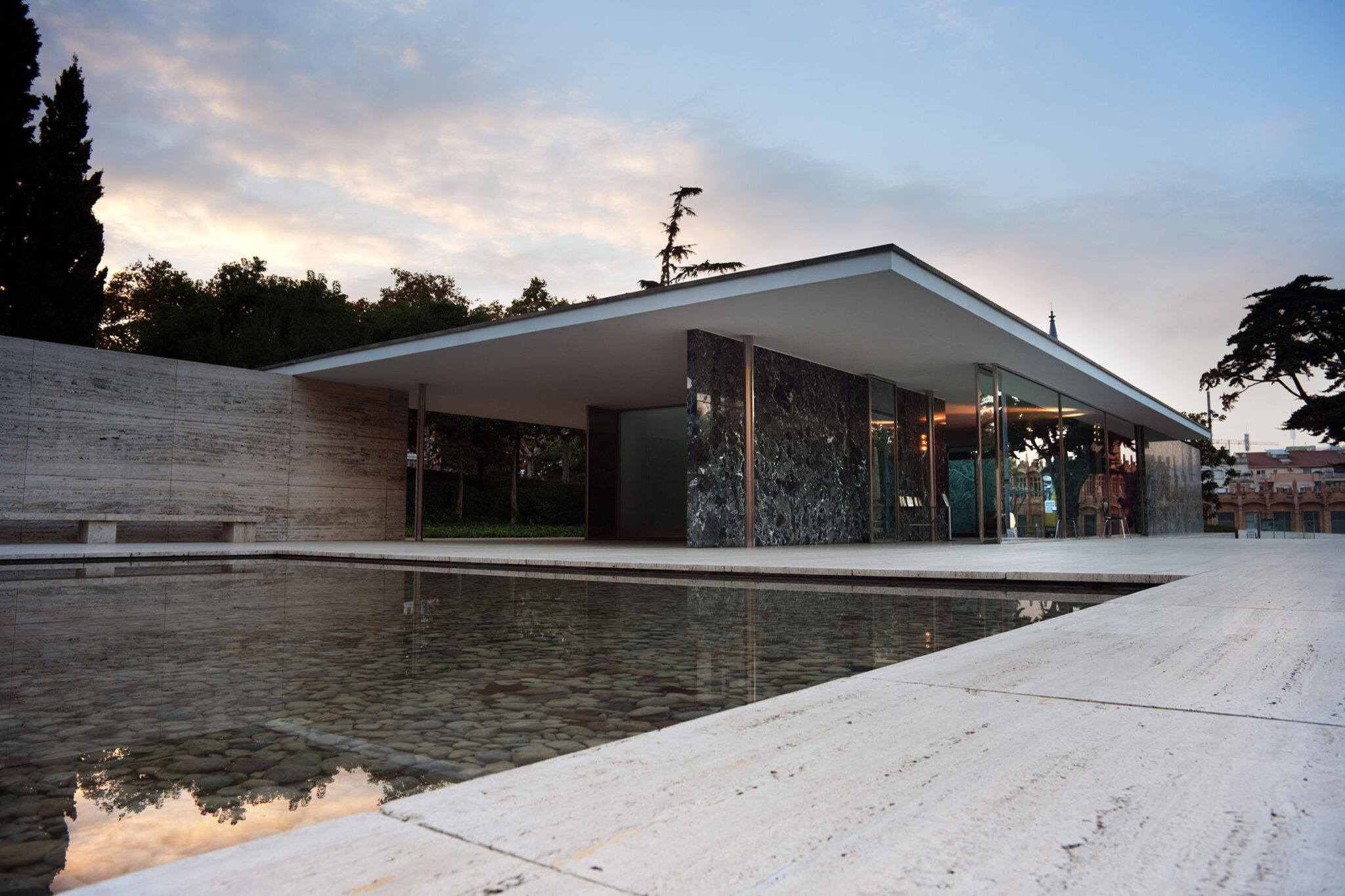 Modern stone-clad building beside a reflective pool at dusk